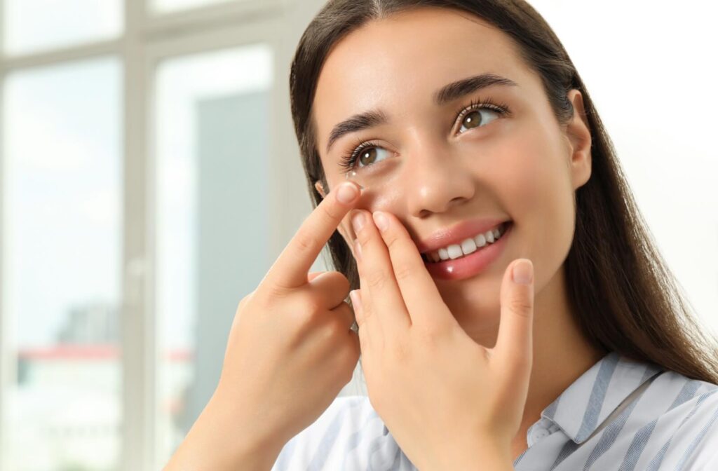 Woman inserting a scleral contact lens into her eye in a bright room.